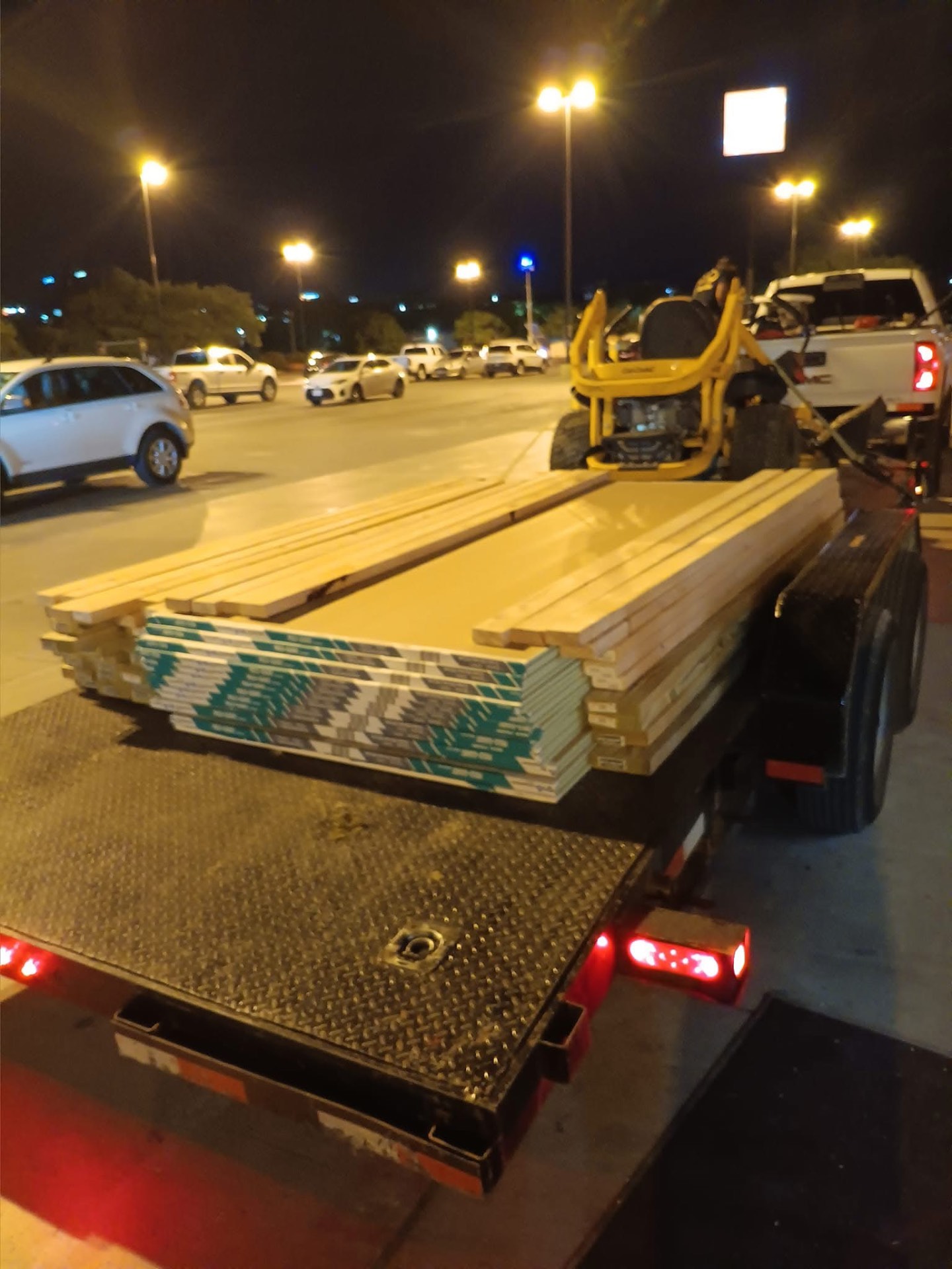 Trailer loaded with lumber and a mower at a late-night material run